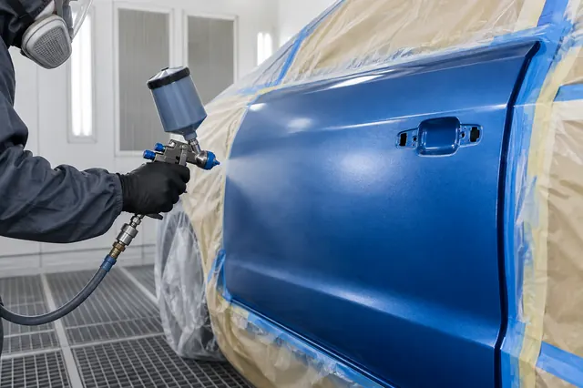 A refinishing technician painting a vehicle panel in a clean spray booth